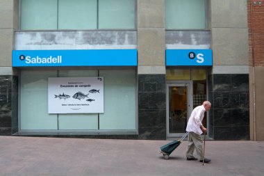 Viladecanlar, Barcelona - 2 Eylül 2025: Bastonlu bir adam sakin bir caddede Sabadell 'deki bir banka şubesinin önünden geçer.