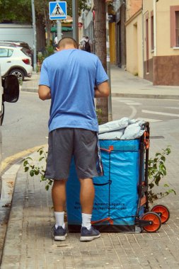 Viladecanlar. Barcelona - Eylül 05, 2025: Arkadan görülen bir Amazon Lojistik sürücüsü, bir caddede yoluna devam etmeden önce katlanabilir teslimat arabasında paketler düzenler..