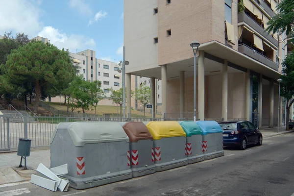 Viladecanlar. Barcelona - Eylül 06, 2025: Değişik renkli kapaklı dört farklı geri dönüşüm konteynırı, kentsel kaldırım kenarına yerleştirilmiştir. Sahne ekolojik farkındalığı artırıyor.