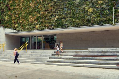 Viladecanlar. Barcelona - 16 Eylül 2025: İnsanlar Viladekan kütüphanesinin önünden çarpıcı dikey bahçesiyle geçiyorlar. Bina sürdürülebilir kentsel tasarım ve modern kamu alanlarını temsil etmektedir..