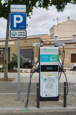 Viladecanlar, Barselona - 17 Eylül 2025: Sokakta bir elektrikli araç şarj istasyonu. Arka planda bir park yeri ve bir bina şehir sahnesini tamamlıyor.