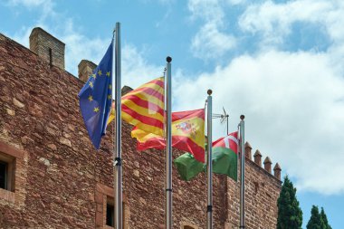 Viladecanlar. Barselona - 18 Eylül 2025: Sallanan bayrakların yakın çekimi, hareketlerini ve renklerini yakalıyor. Arkaplan, tarihi binanın eski bir cephesidir.