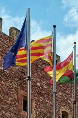 Viladecanlar. Barcelona - 18 Eylül 2025: Avrupa Birliği, Katalonya ve İspanya bayraklarının alçak açılı fotoğrafı. Bayraklar kısmen bulutlu bir gökyüzüne karşı dalgalanıyor