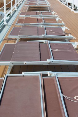 Uzun bir sıra boş kahverengi güneş şezlongları yolcuların güneşlenmeleri ve seyahatleri sırasında dinlenmeleri için hazır olan bir yolcu gemisinin ahşap güvertesinde sıralanır..