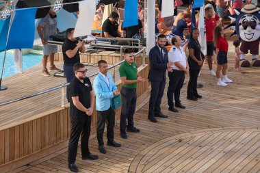 Venedik. İtalya - 24 Eylül 2025: Gezici gemi subayları ve mürettebatı, arka planda eğlenen bir DJ ve yolcuların katıldığı canlı bir parti sırasında havuz güvertesinde tanıtıldı.