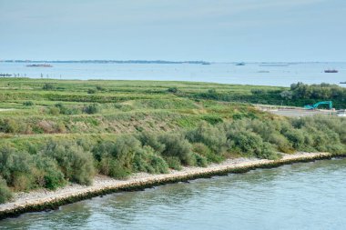 Venedik lagünündeki bir adanın mühendislik ürünü kıyı şeridi, kaya takviyeleri, kıyı bitkileri ve görünür inşaat ekipmanları..