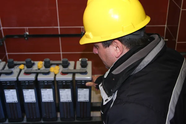 Electricista con acumulador de comprobación de casco amarillo — Foto de Stock