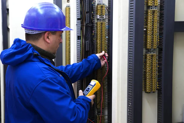 Eletricista em circuito de controle azul com multímetro — Fotografia de Stock