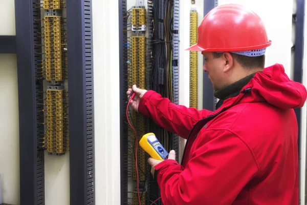 Electricista en circuito de control rojo con multímetro — Foto de Stock