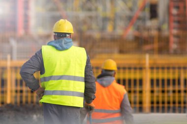 Two workers in yellow and orange at the construction site clipart