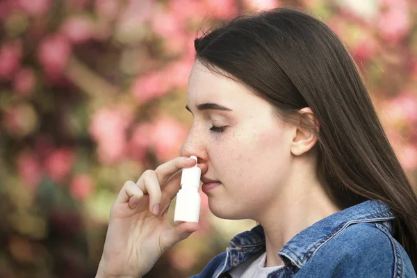 Genç kız pembe çiçek üzerinde parkta burun inhaler kullanarak — Stok fotoğraf