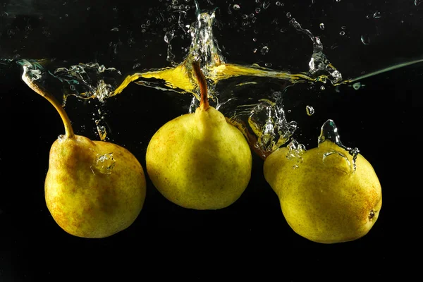 Three pears splashing in water on black