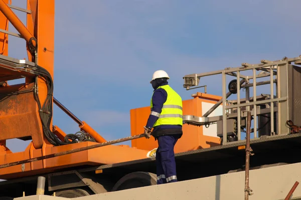Trabajador en grúa amarilla y naranja en el sitio de construcción — Foto de Stock