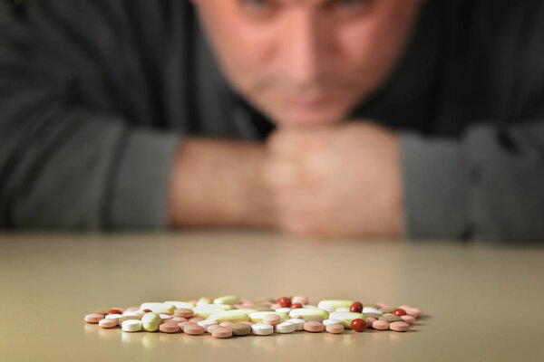 Depressed man beside a lot of colorful pills