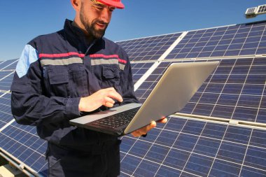 Tehnician kırmızı kasklı ve laptop güneş enerjisi santralinde.