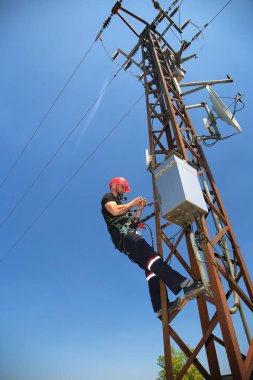 Kırmızı kasklı elektrikçi güç iletim hattı üzerinde çalışıyor.
