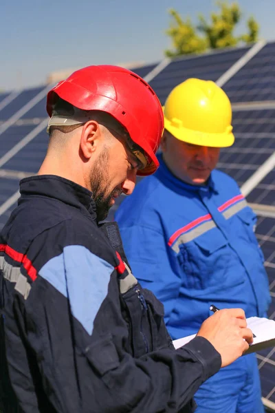Green energy, two workers control solar panels