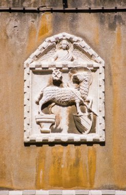 İtalya, Venedik 'te bir duvara oyulmuş eski bir taş levha. Tanrı 'nın kuzusunu bir melek tarafından denetlenen bir bayrak ile göstermek. Yüzlerce yıllık tarihi duvar süslemesi, halka açık kaldırımlardan bakıldığında.