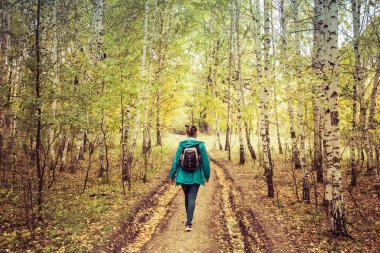 Kız bir sırt çantası ile sonbahar ormanda yürür