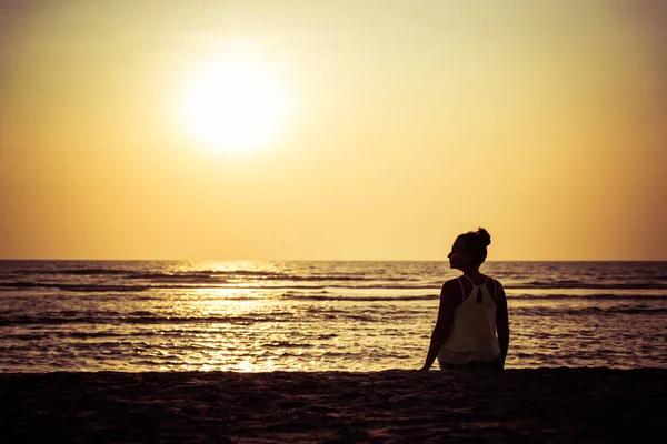 Silueta de una joven mujer contra el telón de fondo de la puesta del sol a — Foto de Stock