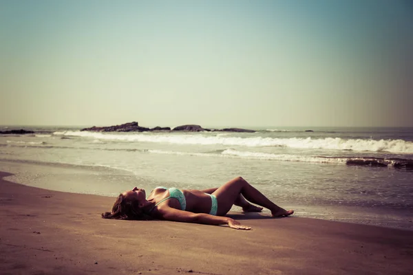 Junge Frau liegt am Strand vor dem Hintergrund des Meeres — Stockfoto