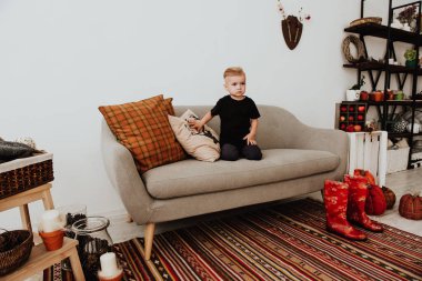 İki yaşındaki havalı hippi çocuk, sonbahar dekorunun süslü fotoğraf sahasında güzel, parlak sonbahar yapraklarıyla poz veriyor. Sıcak atmosfer