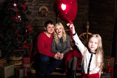 Kırmızılı güzel bir aile Noel tatili için birlikte eğleniyor, oturma odasında yerde oturuyor, güzel dekore edilmiş bir Noel ağacının yanında, gülümsüyor.
