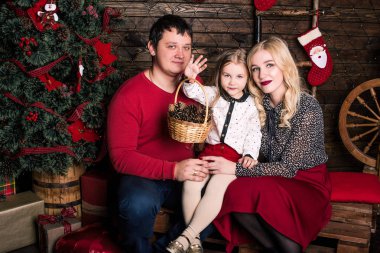 Kırmızılı güzel bir aile Noel tatili için birlikte eğleniyor, oturma odasında yerde oturuyor, güzel dekore edilmiş bir Noel ağacının yanında, gülümsüyor.