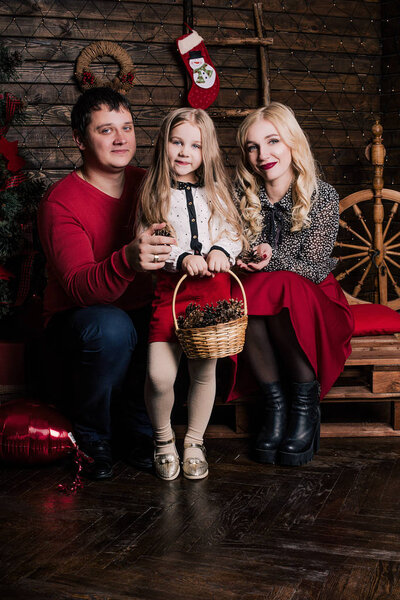 Beautiful young family in red having fun together for Christmas holidays, sitting on a living room floor next to a nicely decorated Christmas tree, smiling