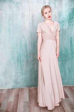 Bej maxi trafo balo Abiye duvardan poz giyen genç kız.