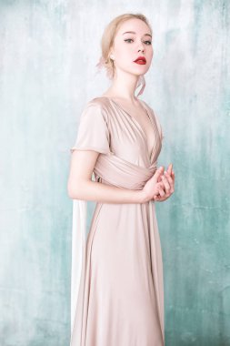 Bej maxi trafo balo Abiye duvardan poz giyen genç kız.