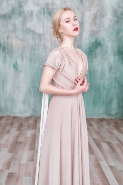 Bej maxi trafo balo Abiye duvardan poz giyen genç kız.