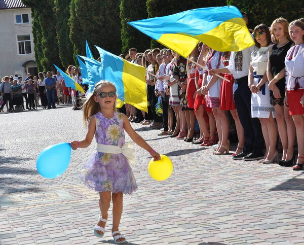 Чертков - Тернополь - Украина - 31 августа 2017 года. Маленькая девочка бегает с мячом на фоне государственных флагов Украины во время торжеств в Государственном педагогическом колледже
 
