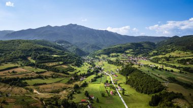 Mavi gökyüzünün altındaki orman tepeleri arasında uzanan yemyeşil bir vadi.