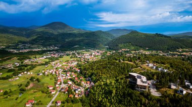 Mavi gökyüzünün altındaki küçük köyü çevreleyen yemyeşil vadi