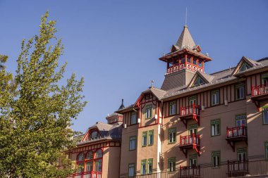 Açık mavi gökyüzünün altında kırmızı balkonların yer aldığı tarihi bina