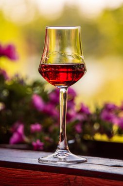 Çiçeklerin yanında kırmızı sıvı tutan zarif şarap kadehleri.