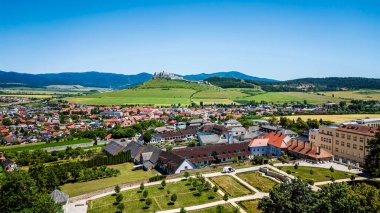 Açık mavi gökyüzünün altındaki yeşil tepeleri çevreleyen renkli çatılar