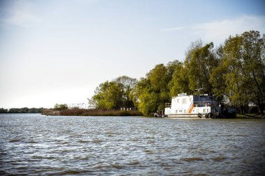 Sakin nehir kıyısında yeşil ağaçların yanında yüzen beyaz yüzen yüzen yüzen yüzen yüzen yüzen ev.