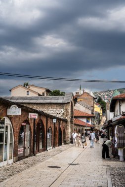 Bulutlu gökyüzü ve yürüyen insanların yer aldığı tarihi sokak sahnesi