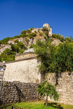 Mavi gökyüzünün altındaki kayalık yeşil yamaçta duran antik taş kale.