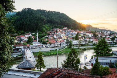 Yeşil tepelerin arasına kurulmuş huzur dolu nehir kenarı köyünü aydınlatan gün batımı.