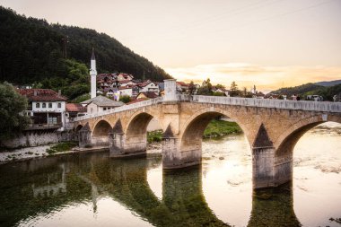 Günbatımında köy evlerinin yakınındaki sakin nehri geçen tarihi taş köprü.