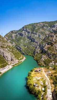 Turkuaz nehri açık gökyüzünün altındaki kayalık yeşil dağların arasından süzülüyor.
