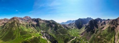 Panoramik manzara açık mavi gökyüzünün altındaki engebeli dağ zirvelerini gösteriyor