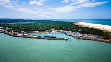Kıyı limanı binalarını gösteren hava manzarası yeşil orman kumlu plajı gösteriyor.