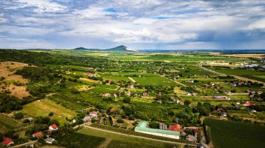 Hava manzarası dağınık evler yeşil arazi tepeleri bulutlu gökyüzünü gösteriyor.