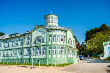 Tarihi yeşil ahşap bina, kumlu sahil yakınlarında birçok pencere var.