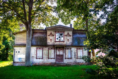 Uzun yeşil ağaçlarla çevrili terk edilmiş ahşap bir ev.