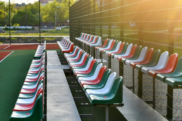 Empty outdoor stadium with red and green seats in sunset light.